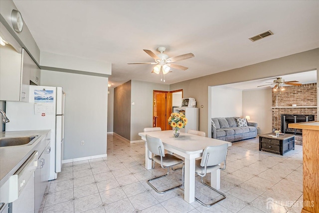 dining area with a ceiling fan, a brick fireplace, visible vents, and baseboards