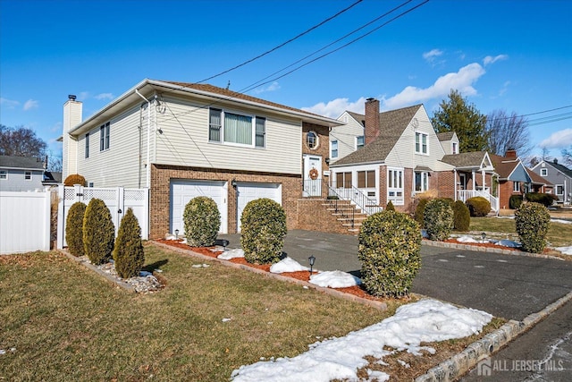 view of front facade with aphalt driveway, brick siding, fence, a residential view, and a front lawn