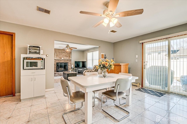 dining room featuring light tile patterned floors, a baseboard radiator, visible vents, a ceiling fan, and a brick fireplace