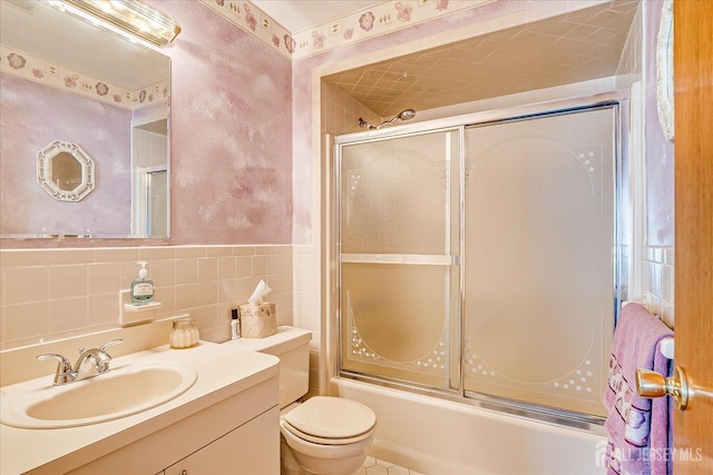 full bath with tile walls, toilet, wainscoting, combined bath / shower with glass door, and vanity