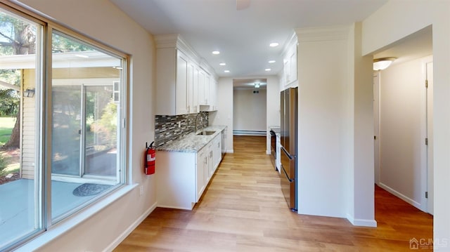 kitchen with white cabinetry, light hardwood / wood-style floors, tasteful backsplash, light stone counters, and sink