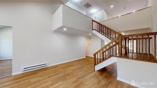 stairway featuring hardwood / wood-style flooring, a baseboard radiator, and a high ceiling