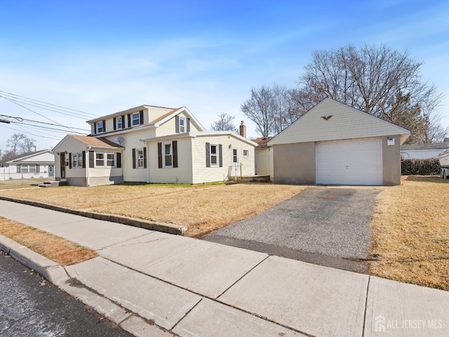 view of front of property with driveway, a detached garage, a front lawn, and an outbuilding