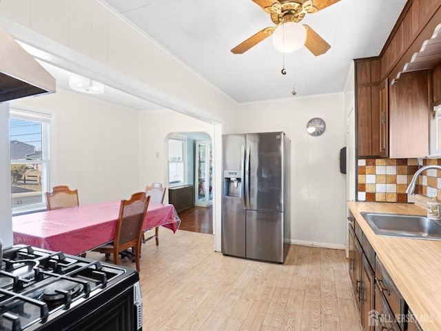 kitchen with crown molding, a sink, black gas range oven, arched walkways, and stainless steel refrigerator with ice dispenser