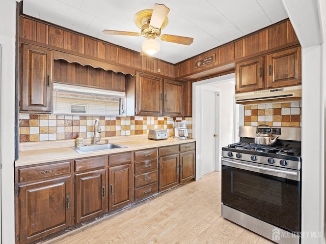 kitchen with gas stove, under cabinet range hood, light countertops, backsplash, and a sink