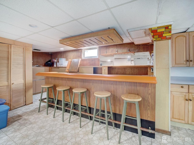 451 Burroughs Ter, Union Twp, NJ 07083 - kitchen with light brown cabinetry, a breakfast bar, light floors, a paneled ceiling, and wooden walls
