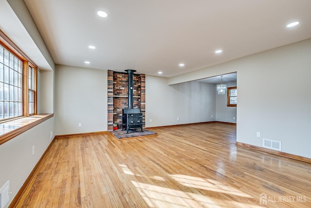 unfurnished living room with recessed lighting, visible vents, a wood stove, light wood-type flooring, and baseboards