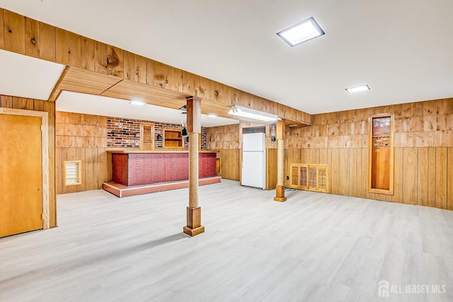 finished basement with wood walls, wood finished floors, and freestanding refrigerator