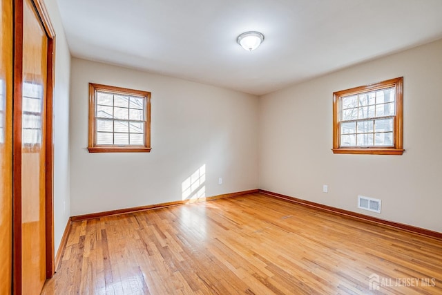 empty room with baseboards, visible vents, and light wood finished floors