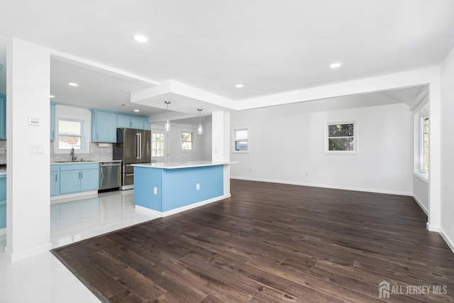 kitchen with blue cabinetry, stainless steel appliances, decorative light fixtures, a kitchen island, and sink