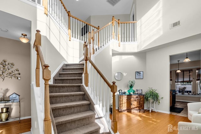 stairs featuring a towering ceiling, baseboards, visible vents, and wood finished floors