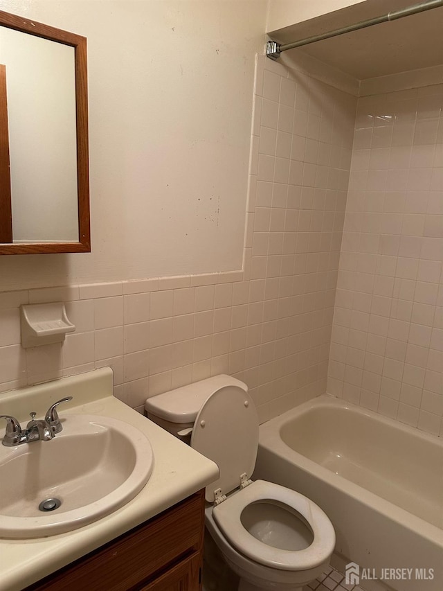 full bath featuring washtub / shower combination, toilet, vanity, wainscoting, and tile walls