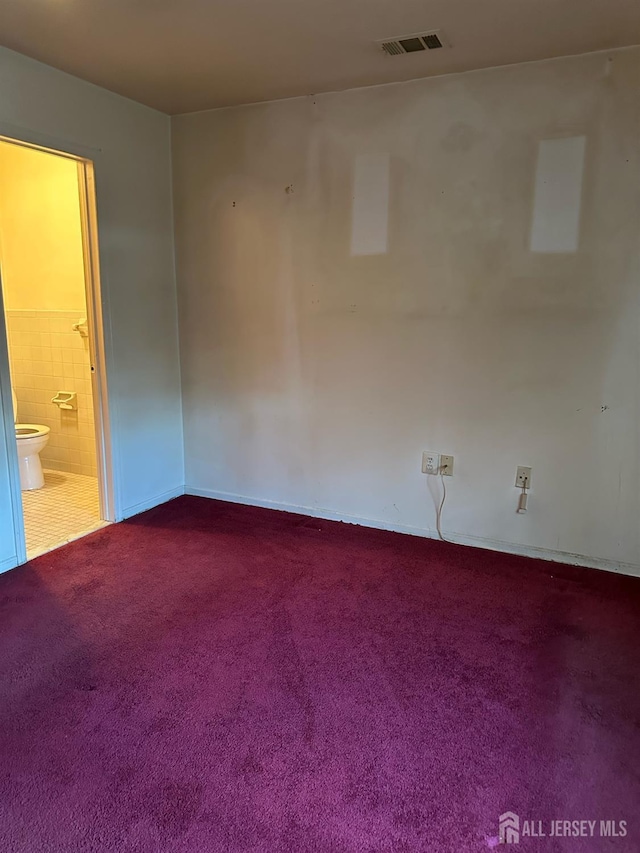 unfurnished room with visible vents, dark carpet, and tile walls