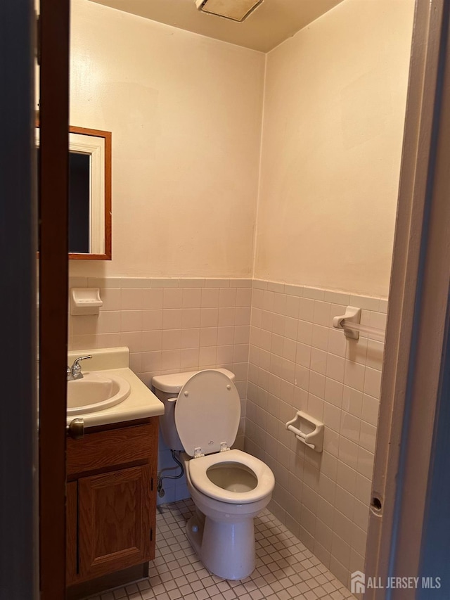 bathroom featuring tile patterned floors, toilet, tile walls, and wainscoting