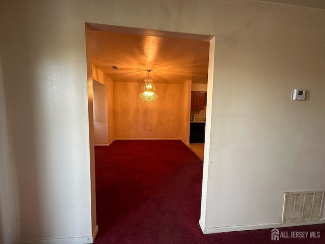 corridor featuring dark colored carpet, visible vents, and baseboards