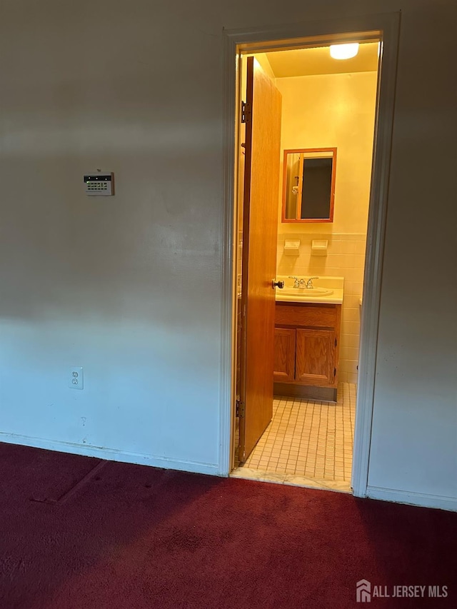 hall featuring light colored carpet, tile walls, and a sink