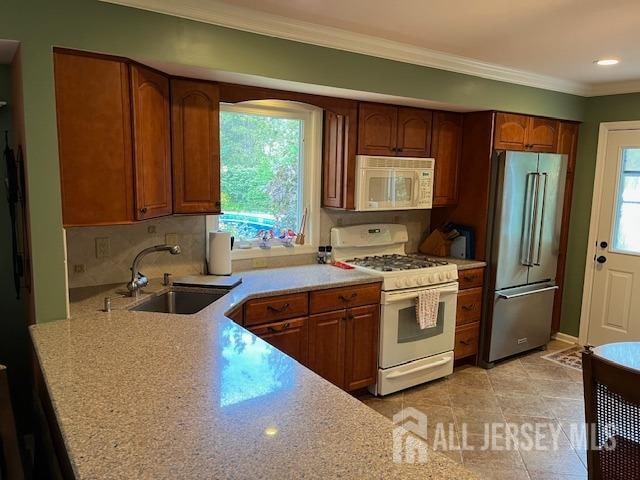 kitchen featuring white appliances, tasteful backsplash, light stone countertops, sink, and ornamental molding