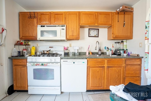 kitchen with brown cabinets, dark countertops, light tile patterned flooring, a sink, and white appliances