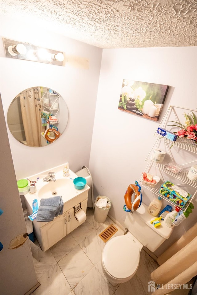 bathroom featuring marble finish floor, toilet, vanity, and a textured ceiling