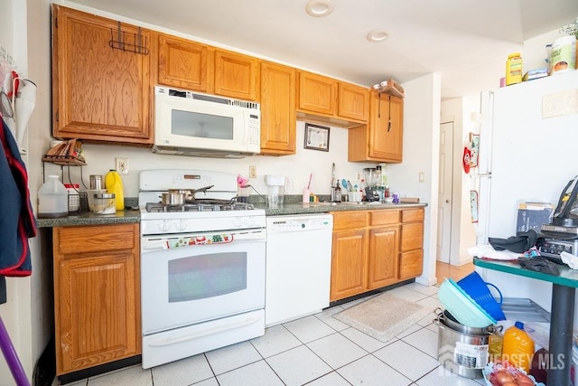 kitchen with brown cabinets, dark countertops, white appliances, and light tile patterned flooring