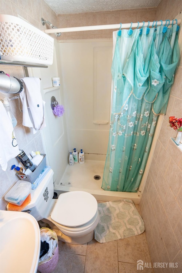 full bath featuring a stall shower, toilet, tile patterned flooring, a textured ceiling, and a sink