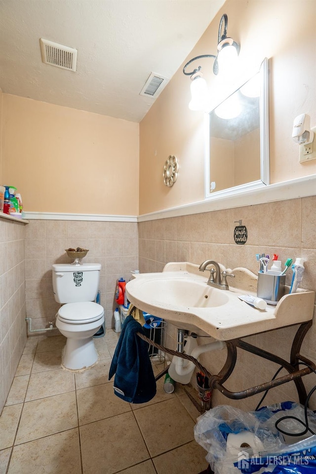 half bathroom featuring toilet, tile patterned flooring, visible vents, and tile walls