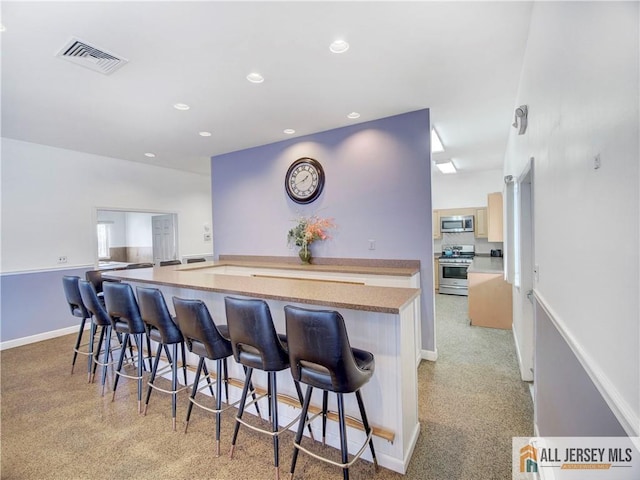 kitchen with light brown cabinetry, a breakfast bar area, stainless steel appliances, and a center island