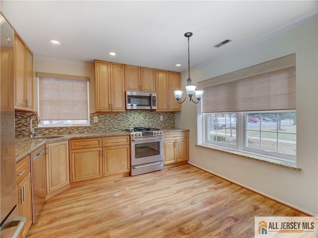 kitchen featuring appliances with stainless steel finishes, decorative light fixtures, sink, decorative backsplash, and light hardwood / wood-style flooring