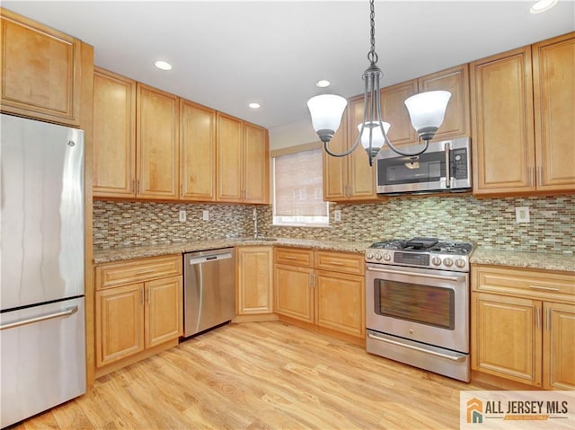 kitchen with pendant lighting, stainless steel appliances, decorative backsplash, and light wood-type flooring