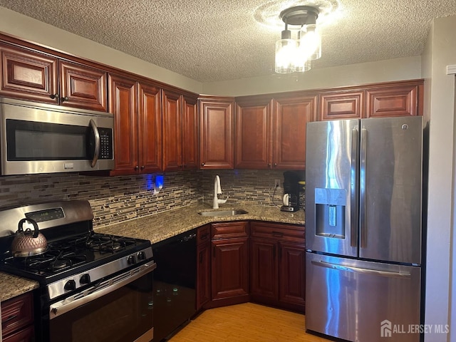 kitchen featuring tasteful backsplash, a sink, a textured ceiling, light wood finished floors, and appliances with stainless steel finishes