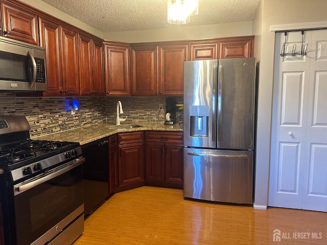 kitchen with sink, appliances with stainless steel finishes, light stone countertops, light hardwood / wood-style floors, and decorative backsplash