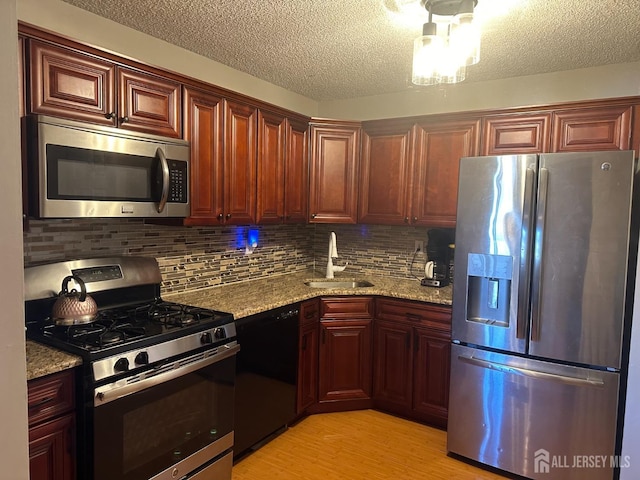 kitchen with light stone countertops, stainless steel appliances, light hardwood / wood-style flooring, and sink