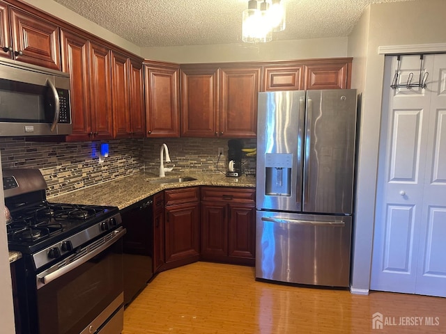 kitchen with sink, light hardwood / wood-style flooring, stainless steel appliances, light stone counters, and tasteful backsplash