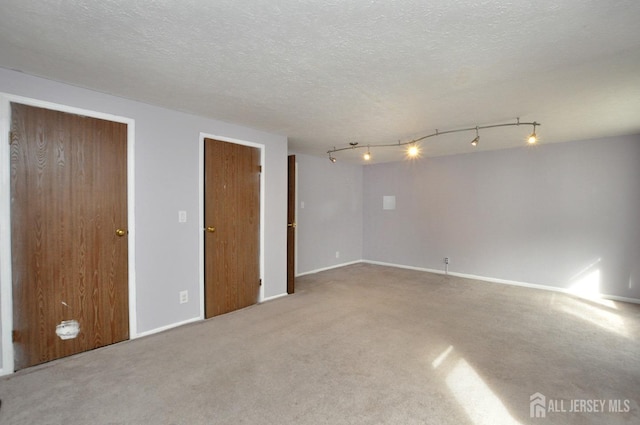 spare room featuring carpet floors, a textured ceiling, and track lighting