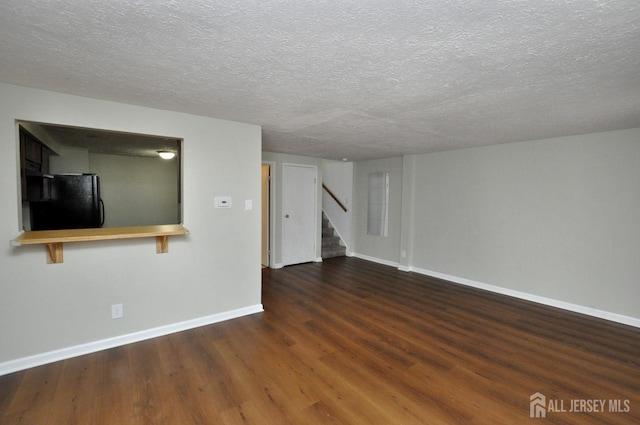 unfurnished living room with wood finished floors, a textured ceiling, baseboards, and stairs