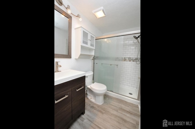 bathroom featuring wood-type flooring, toilet, an enclosed shower, and vanity