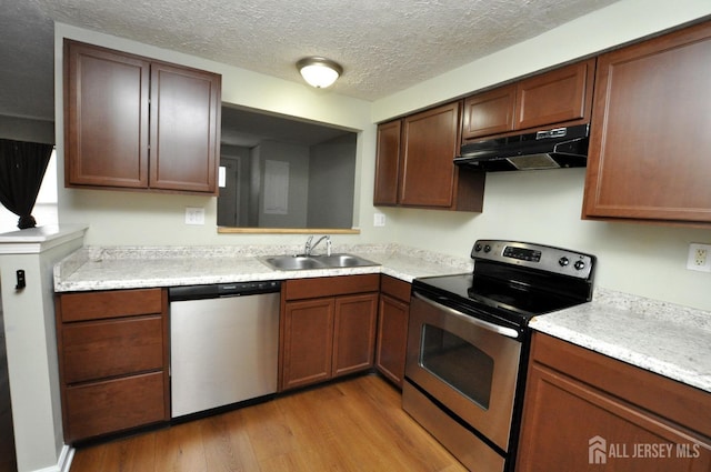 kitchen featuring stainless steel appliances, sink, a textured ceiling, and light wood-type flooring