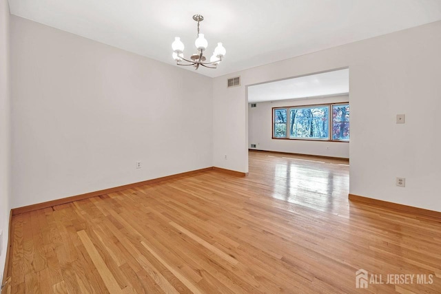 empty room featuring visible vents, a notable chandelier, light wood-style flooring, and baseboards