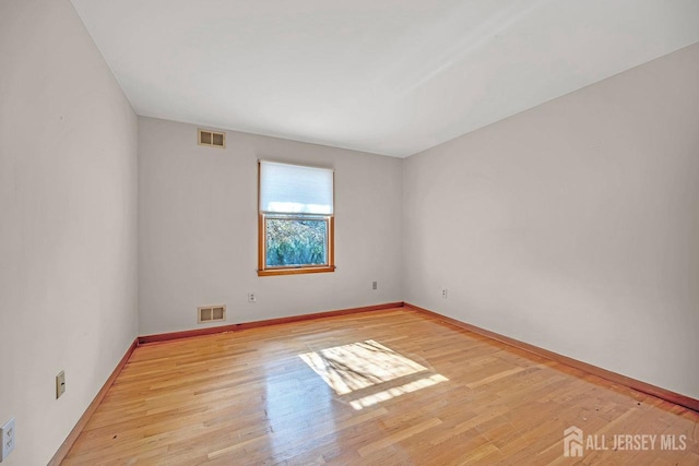 empty room featuring light wood-style flooring, visible vents, and baseboards