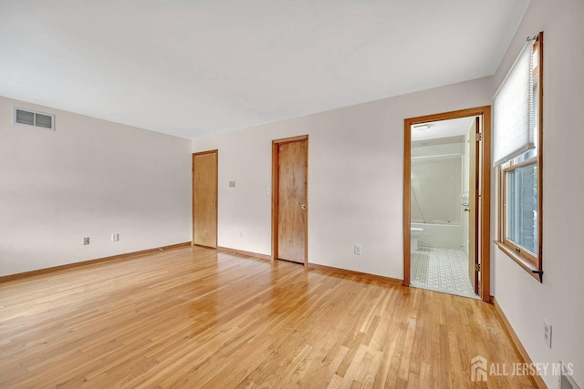 unfurnished bedroom featuring baseboards, visible vents, connected bathroom, light wood-style floors, and two closets