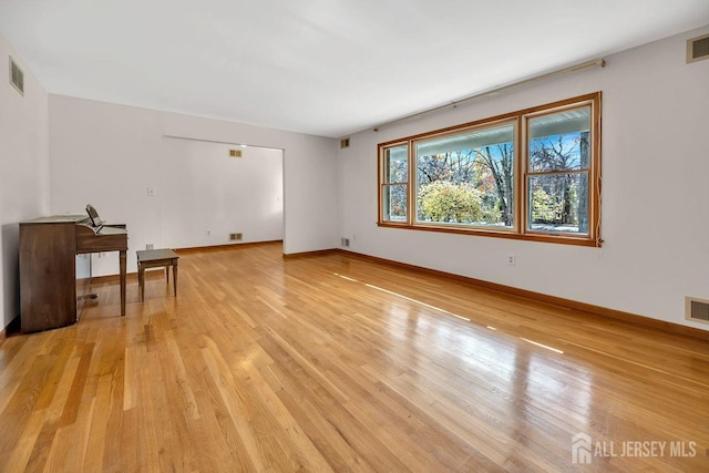 empty room with baseboards, visible vents, and light wood finished floors