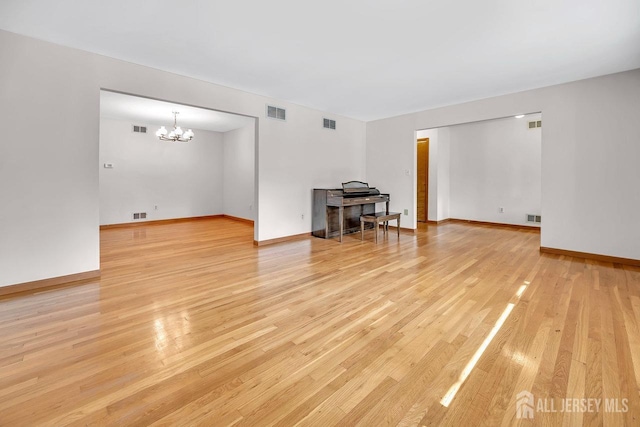 unfurnished living room with light wood-type flooring, visible vents, and a chandelier