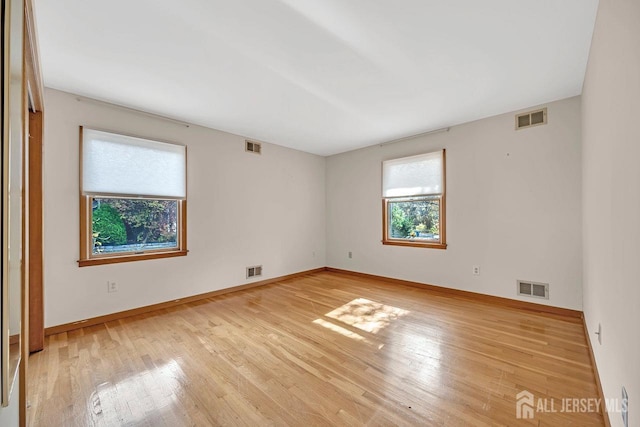 spare room with light wood finished floors, visible vents, and baseboards