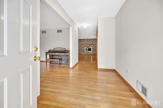 foyer entrance with a brick fireplace, visible vents, and light wood finished floors