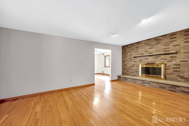 unfurnished living room featuring light wood finished floors, a brick fireplace, and baseboards