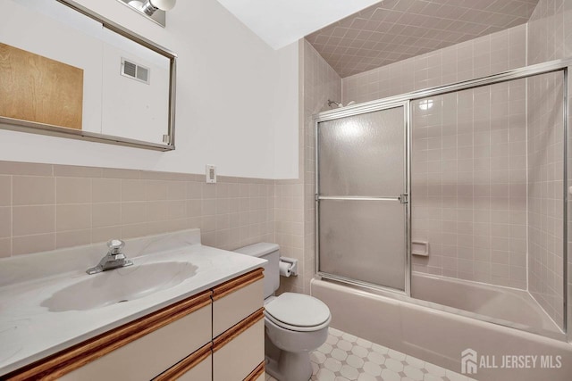 full bathroom with toilet, shower / bath combination with glass door, tile patterned floors, vanity, and tile walls