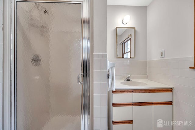 bathroom with vanity, wainscoting, a shower stall, and tile walls