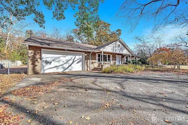 view of front of house featuring covered porch, driveway, brick siding, and a garage