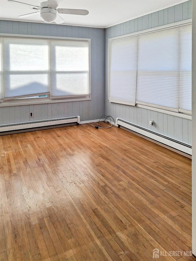 spare room with wooden walls, light hardwood / wood-style flooring, ceiling fan, and a baseboard heating unit