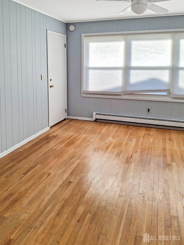 unfurnished room featuring wooden walls, ceiling fan, a baseboard radiator, and light hardwood / wood-style floors